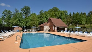 Une piscine rectangulaire entourée d’un bâtiment en bois et d’arbres, avec des chaises longues et des parasols.