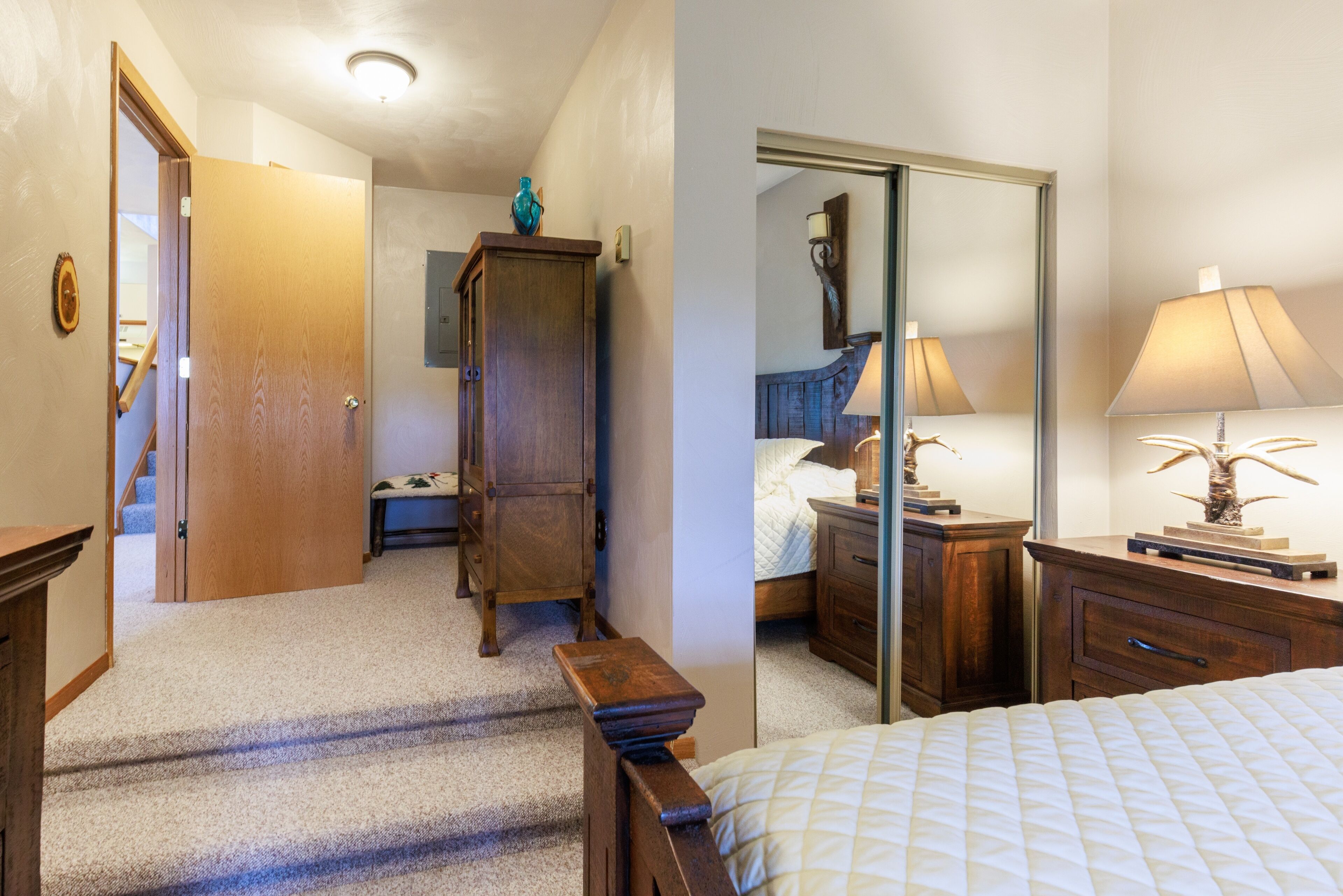A bedroom with a bed, a wooden nightstand, a dresser, a mirror, and a door leading to a hallway.