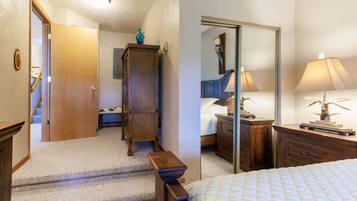 A bedroom with a bed, a wooden nightstand, a dresser, a mirror, and a door leading to a hallway.