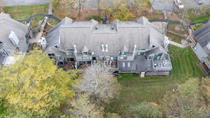 Vue aérienne d’une grande maison moderne à l’architecture symétrique, dotée de nombreuses cheminées et d’une pelouse bien entretenue.