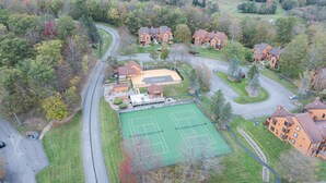 Vue aérienne d’un quartier résidentiel avec un court de tennis, des maisons et une route sinueuse.