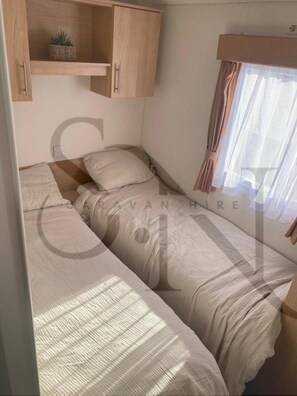 Ein kleines Zimmer mit einem Einzelbett, einem Holzschrank und einem Fenster mit Vorhängen.