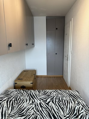 A bedroom with a zebra-patterned bed, a wooden chest, grey wardrobe, and a white door. - Lovely Apartment in Valley and Hills (Veysonnaz)
