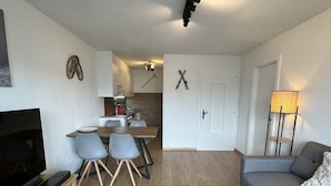 Een moderne woonkamer met een grijze bank, een tv-meubel en een eethoek met een houten tafel en stoelen.