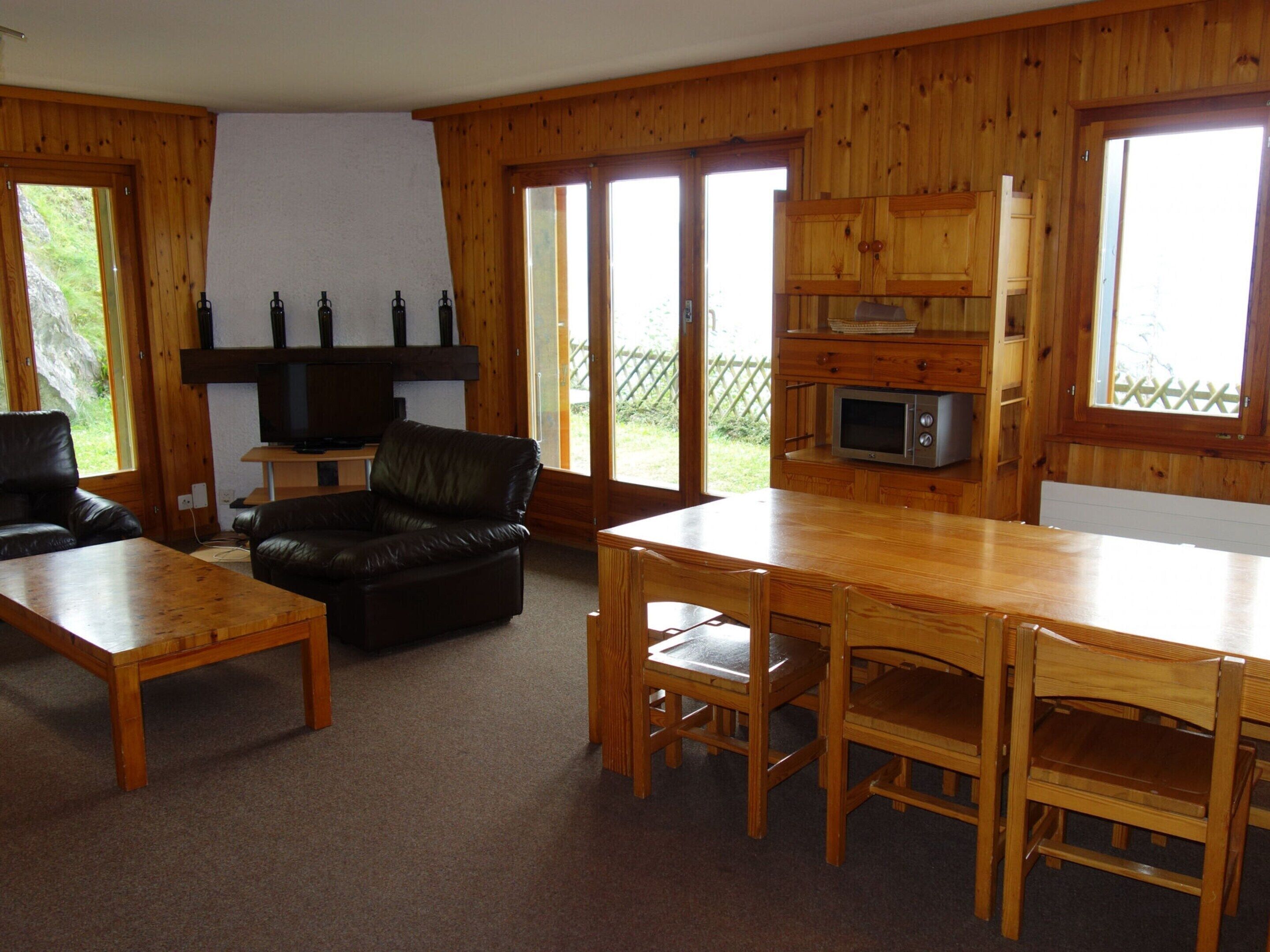 A wooden interior with a sofa, a dining table, and a TV.