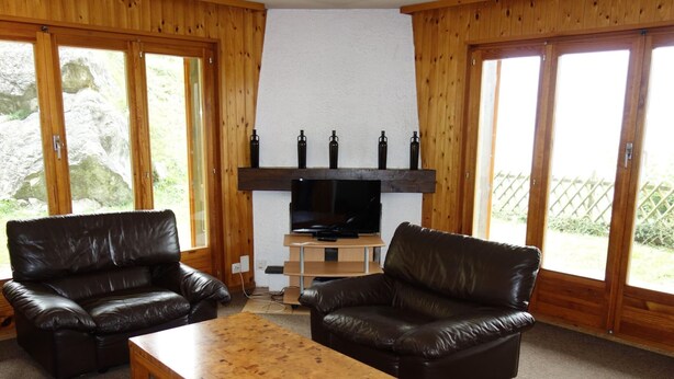 A cozy living room with two leather sofas, a wooden coffee table, and a TV on a wooden stand. - Stunning Apartment With Mountain Views (Veysonnaz)