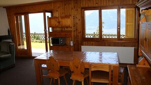 A wooden kitchen with a dining table and chairs, a microwave, and a view of mountains through large windows. - Stunning Apartment With Mountain Views (Veysonnaz)