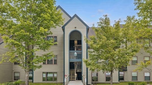A multi-story building with a central entrance, a covered walkway, and a small outdoor area with trees. - Gorgeous 3BR Ski-In/Ski-Out Condo at Okemo (Ludlow)