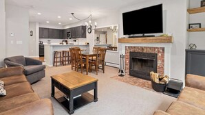 A modern living room with a fireplace, a dining area, and a kitchen in the background. - Gorgeous 3BR Ski-In/Ski-Out Condo at Okemo (Ludlow)