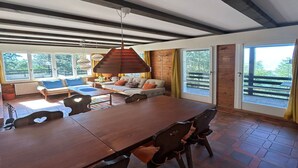 A spacious room with a large wooden dining table, comfortable seating, and a view of the outdoors through large windows. - Cache-cache Mountain & Quiet Chalet 10 Pers (Nendaz)