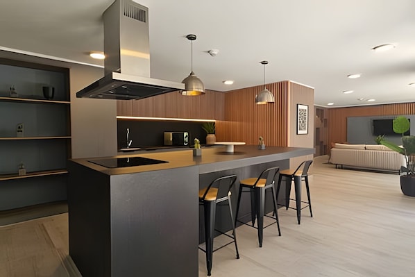 Una cocina moderna con una isla central, taburetes de bar, iluminación colgante y horno empotrado.