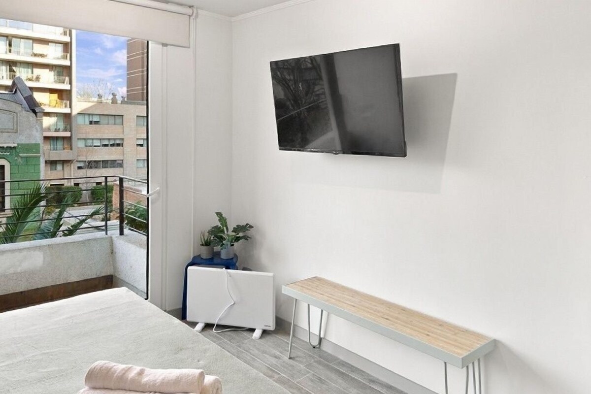 Une chambre à coucher moderne avec un lit, un banc, un radiateur et un téléviseur fixé au mur.