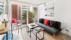 Un salon moderne avec un canapé, un fauteuil, une table basse et un balcon offrant une vue sur les immeubles.