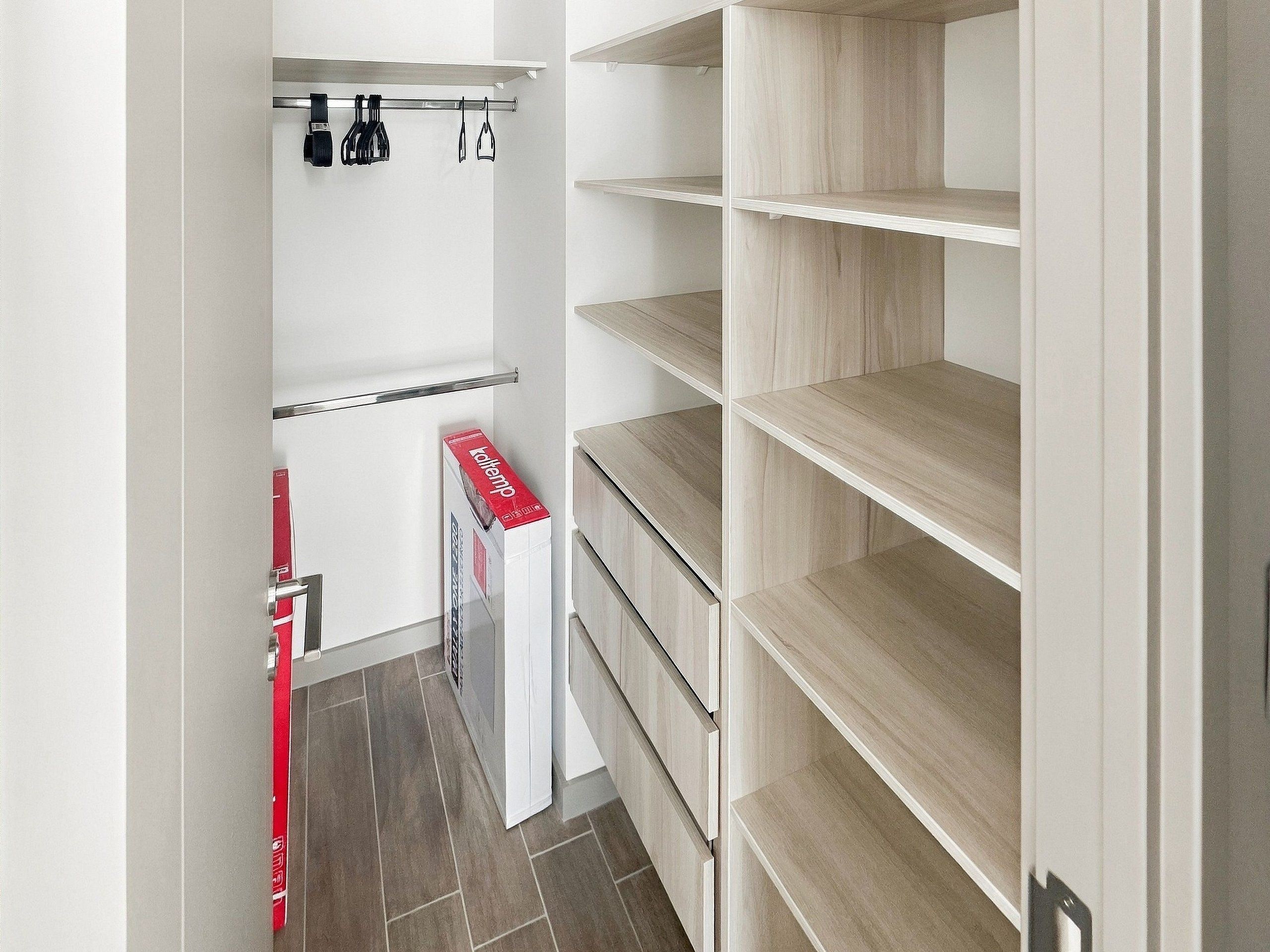 A storage closet with shelves and hanging space, a red box on the floor, and a door with a handle.