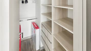 A storage closet with shelves and hanging space, a red box on the floor, and a door with a handle.