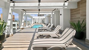 A rooftop pool area with sun loungers and potted plants.