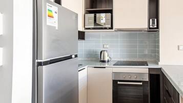Una cocina compacta con refrigerador de acero inoxidable, microondas, tetera y horno empotrado.