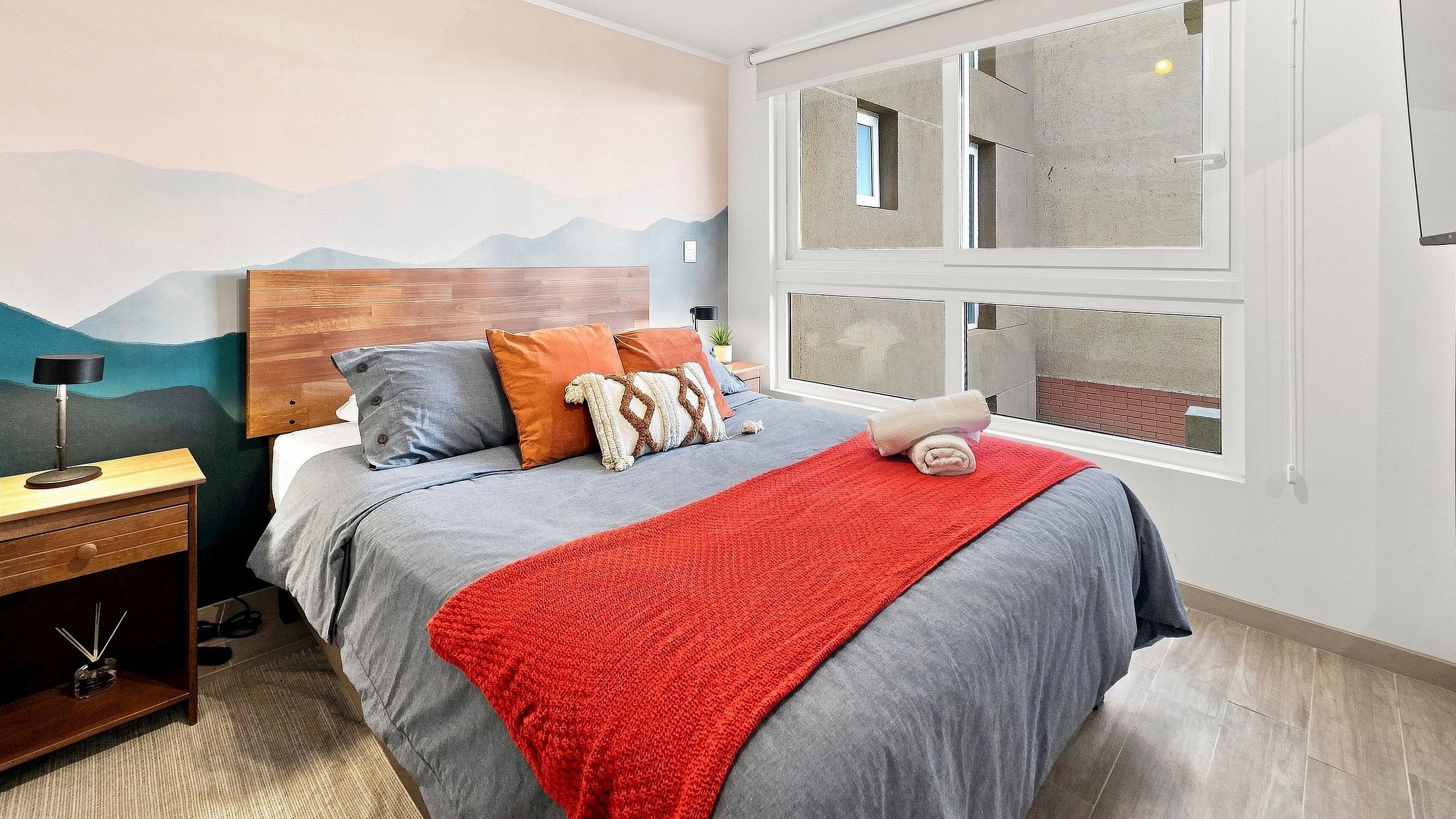 Une chambre à coucher avec un lit, une table de chevet, une lampe et une fenêtre donnant sur un beau paysage.