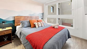 Quarto com cama, mesa de cabeceira, luminária e janela com vista.