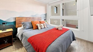 Ein Schlafzimmer mit einem Bett, einem Nachttisch, einer Lampe und einem Fenster mit Blick.