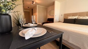 Une chambre d’hôtel avec un lit soigneusement fait, une table à manger avec des assiettes et un verre, et un vase rempli de fleurs.