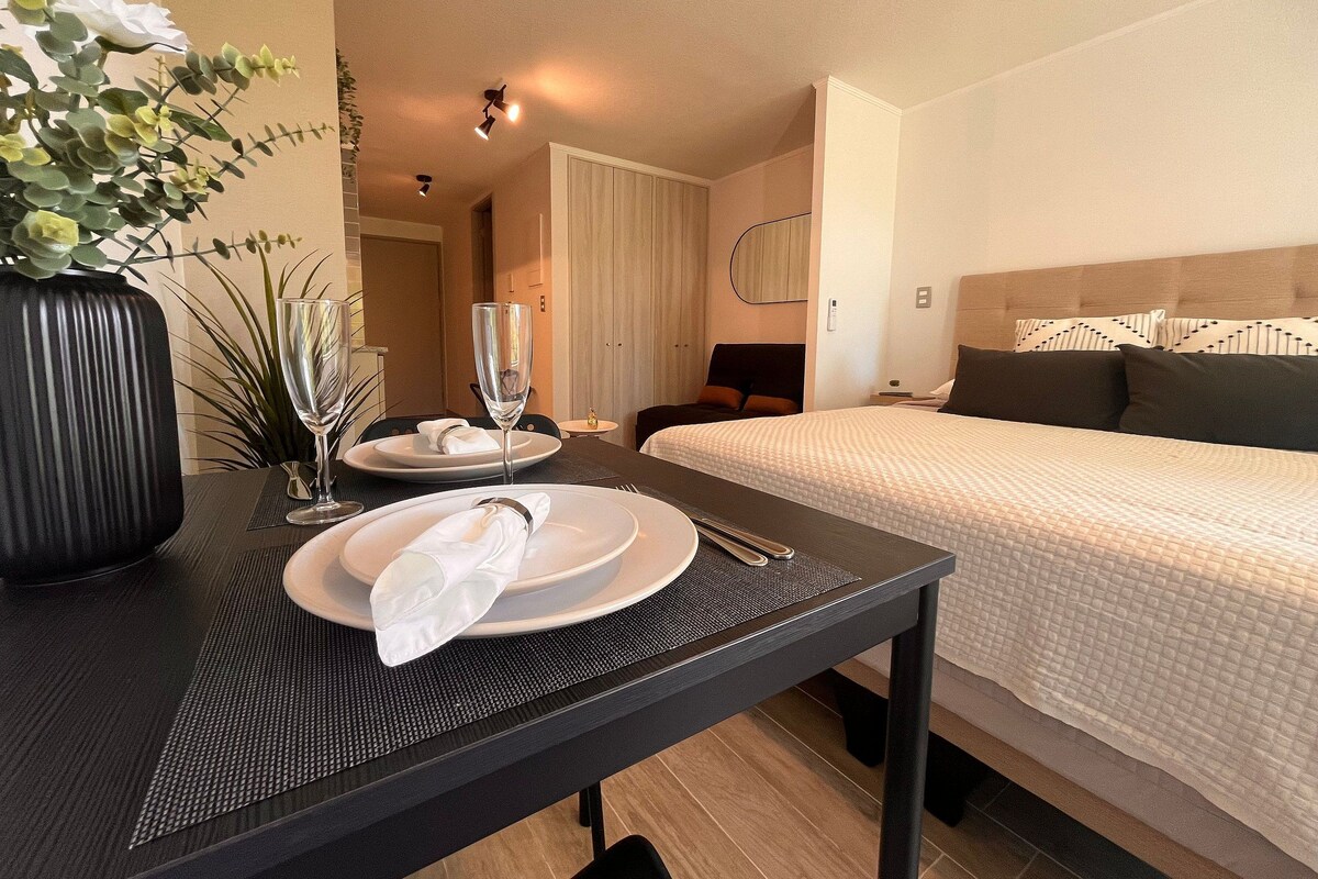 Une chambre d’hôtel avec un lit soigneusement fait, une table à manger avec des assiettes et un verre, et un vase rempli de fleurs.