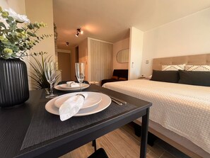 Une chambre d’hôtel avec un lit soigneusement fait, une table à manger avec des assiettes et un verre, et un vase rempli de fleurs.