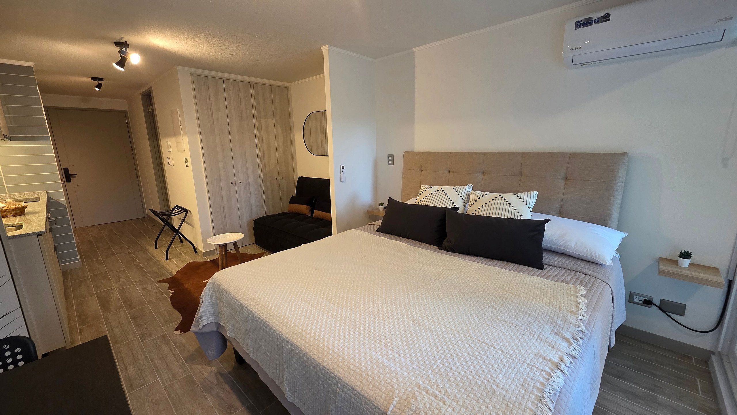 Un dormitorio con cama, mesita de noche, silla y equipo de aire acondicionado.