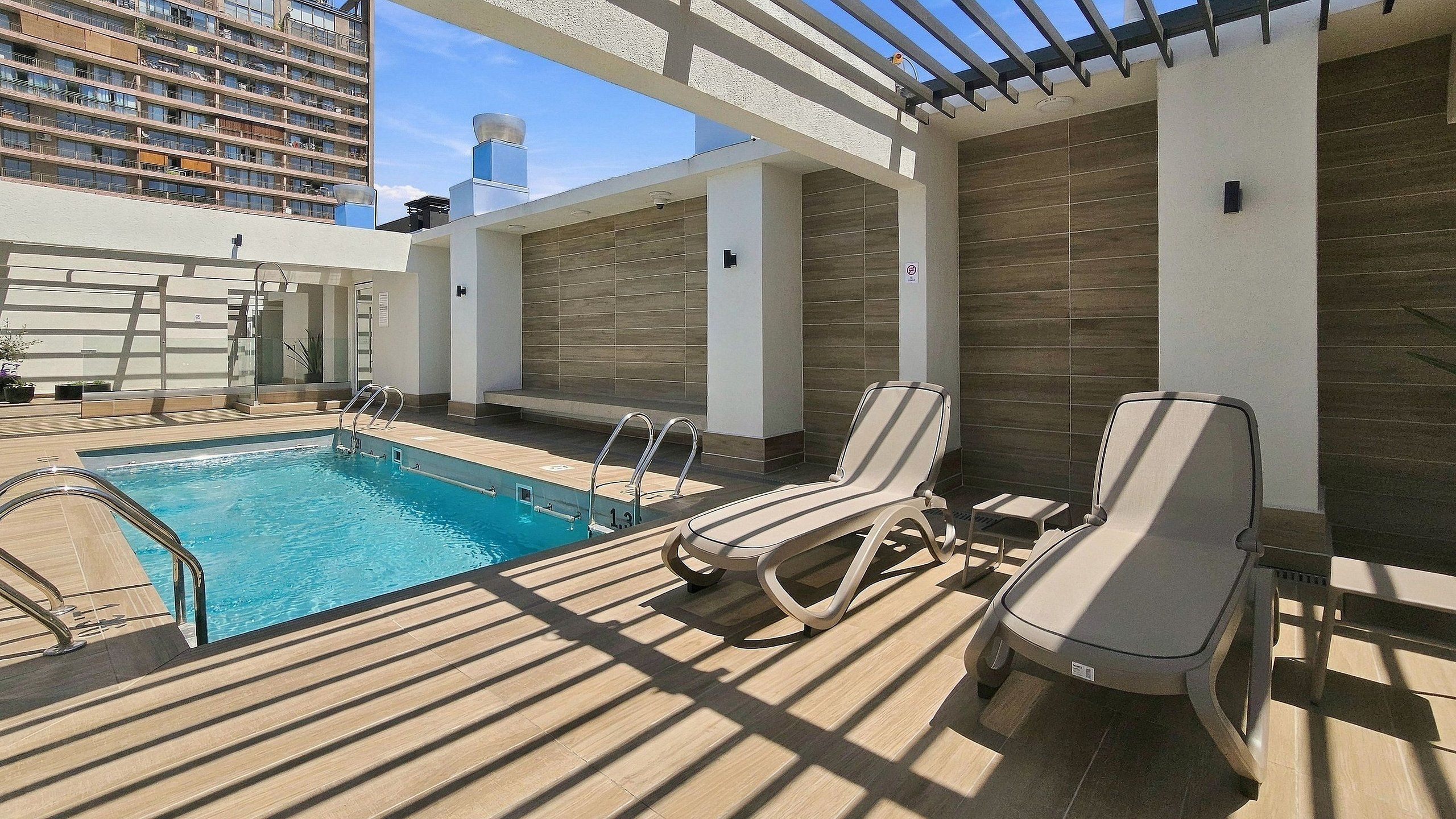 A rooftop pool area with a clear blue pool, sun loungers, and a pergola structure.