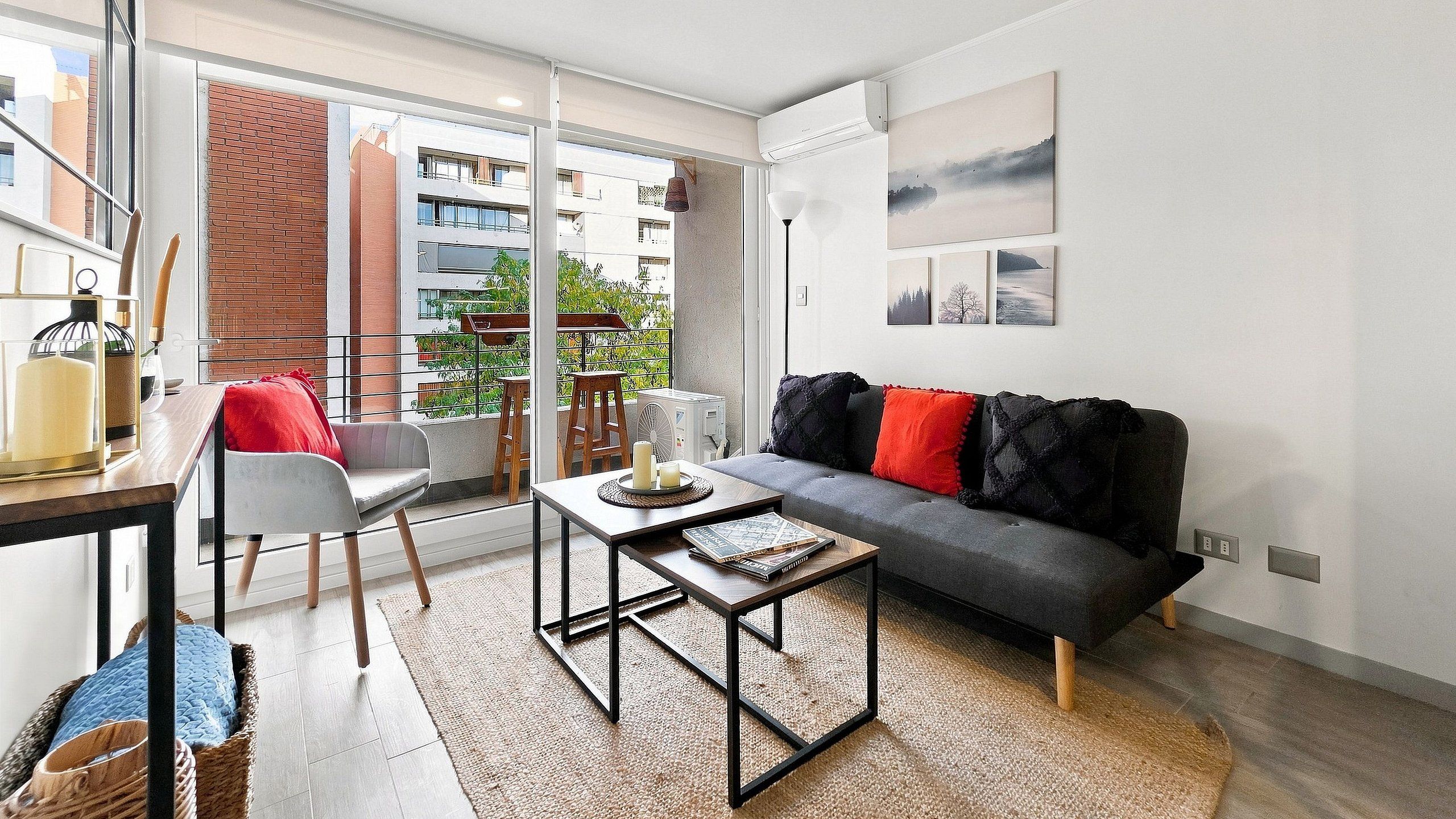 Una sala de estar moderna con un sofá gris, una mesa de centro de madera y un cojín decorativo con estampado rojo y negro.