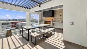 An outdoor terrace with a table and benches, a flat-screen TV mounted on a wooden wall, and a view of the cityscape.