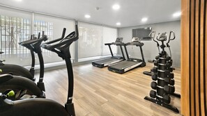 Une salle de sport à domicile équipée de matériel d’exercice, notamment un tapis de course, un vélo elliptique et des haltères.
