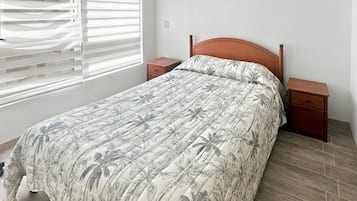 Un dormitorio con una cama, mesitas de noche, una ventana con persianas y suelo de madera.