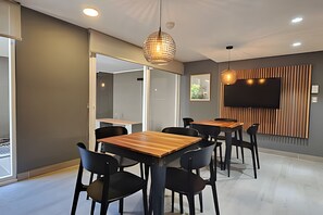 Een moderne vergaderruimte met houten tafels en zwarte stoelen, een groot flatscreentelevisie aan de muur en in het plafond ingebouwde verlichting.