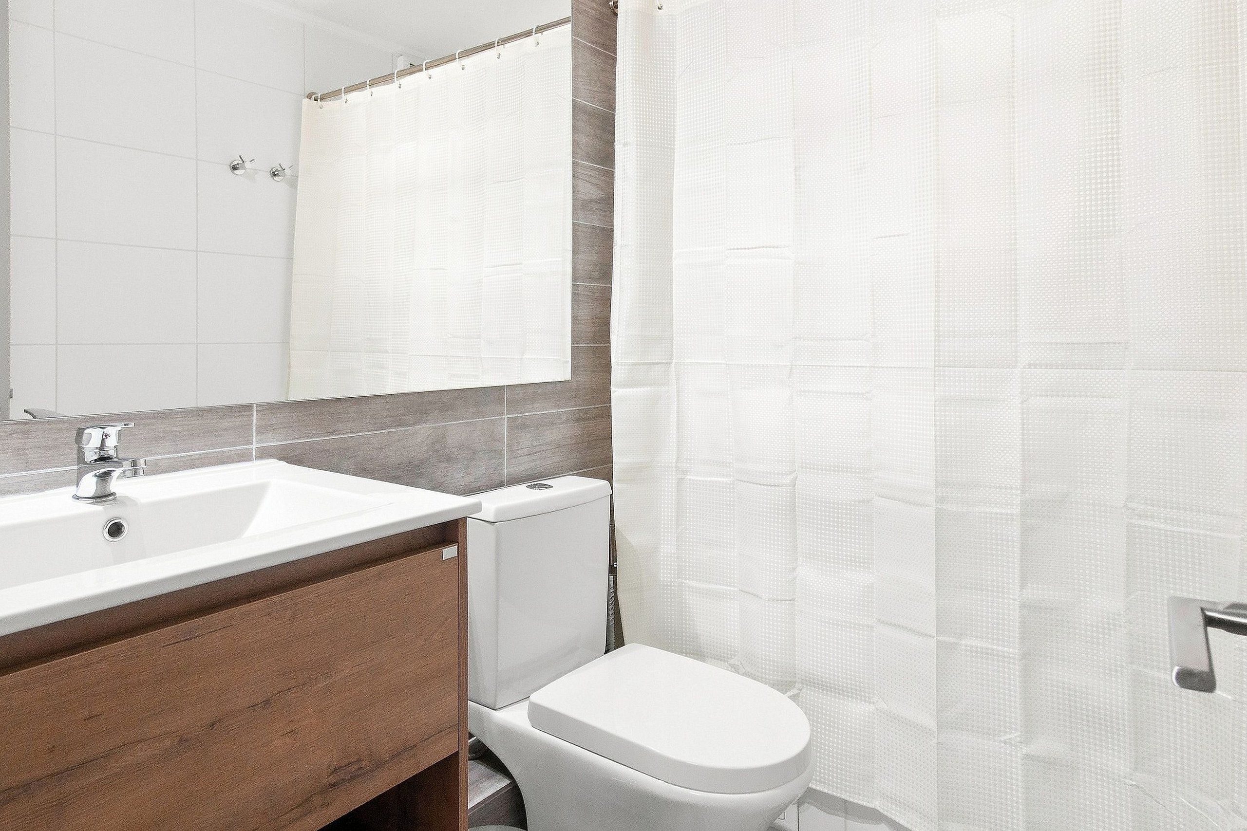 Un baño con lavamanos blanco, un espejo, inodoro y cortina de ducha.