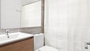 A bathroom with a white sink, a mirror, a toilet, and a shower curtain. - Oceana Suites Eco España (Santiago)