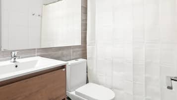 Un baño con lavamanos blanco, un espejo, inodoro y cortina de ducha.