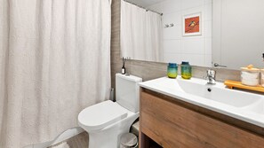 A bathroom with a white toilet, a wooden vanity, a mirror, and a shower curtain.