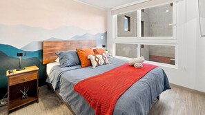Een slaapkamer met een bed, een nachtkastje, een lamp, een raam met uitzicht en een muur met een bergdecoratie.