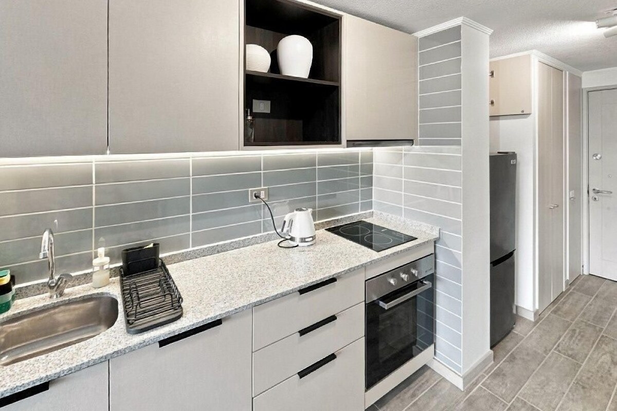 A modern kitchen with grey cabinets, a built-in oven, and a countertop with a kettle.