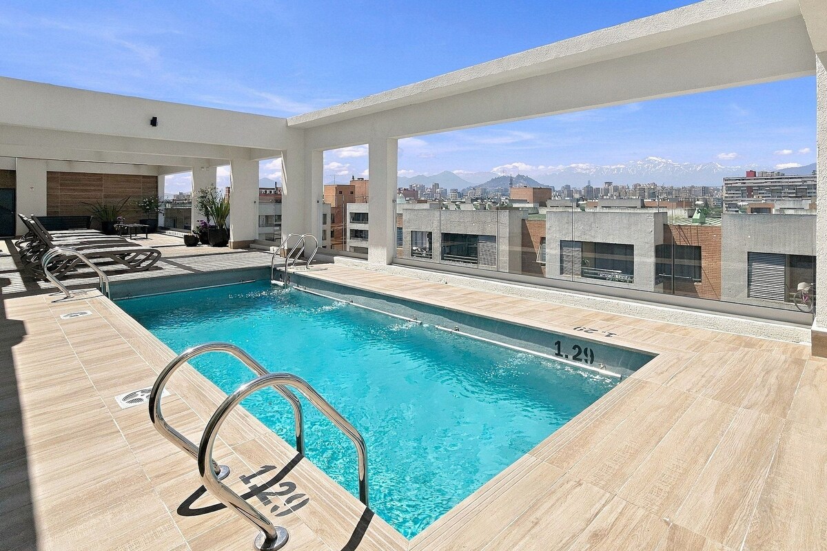 Une piscine sur le toit, avec une eau d’un bleu cristallin, entourée d’une terrasse en bois et de rampes en métal.