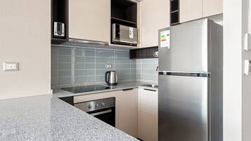 Cozinha moderna com eletrodomésticos de aço inoxidável, micro-ondas e chaleira sobre a bancada.