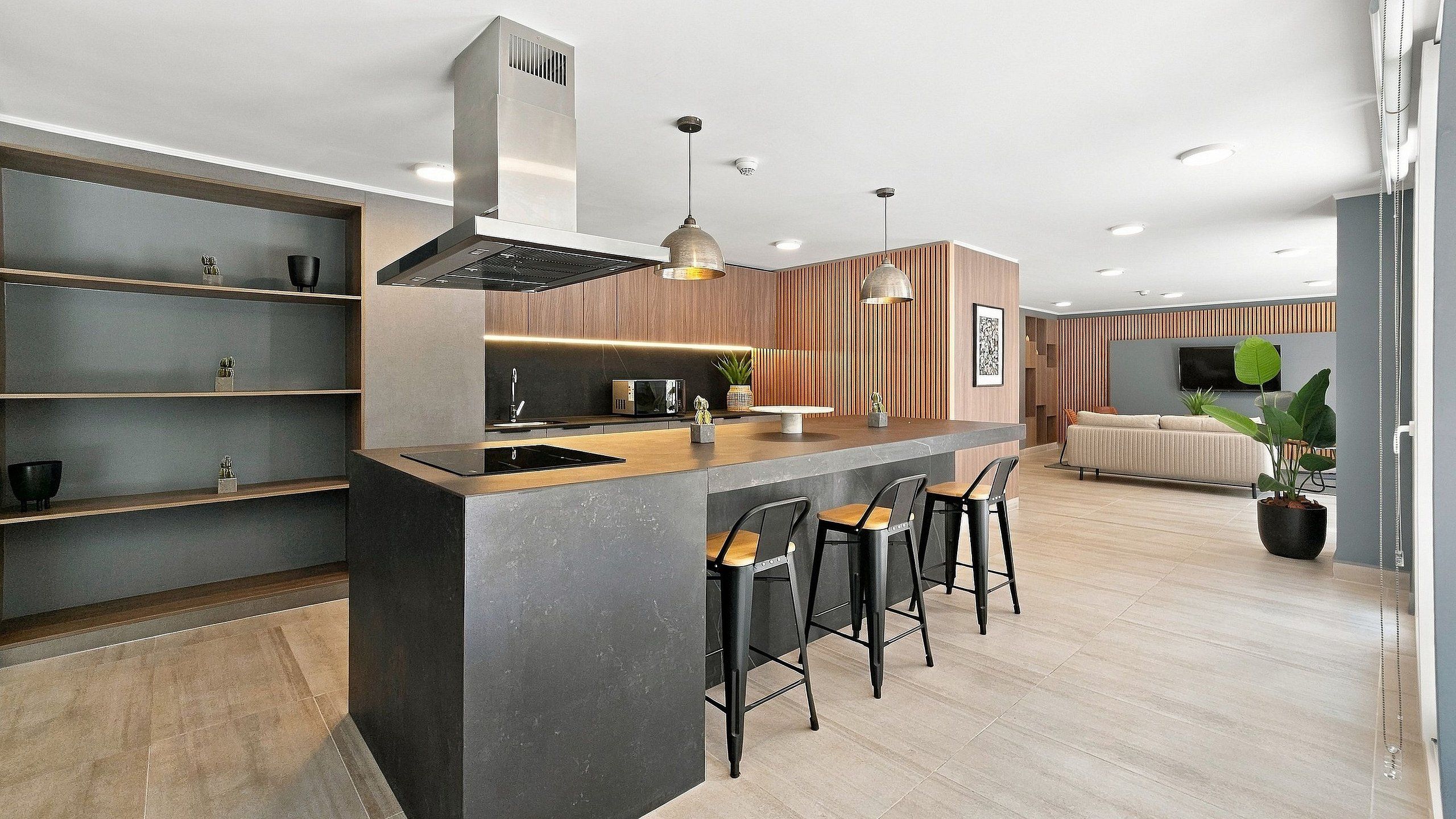 Una cocina moderna con una isla central, taburetes de bar y un comedor con sofá y televisor.