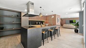 Una cocina moderna con una isla central, taburetes de bar y un comedor con sofá y televisor.