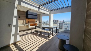 Une terrasse sur le toit équipée d’une table à manger, de chaises, d’une petite table ronde et d’un barbecue.
