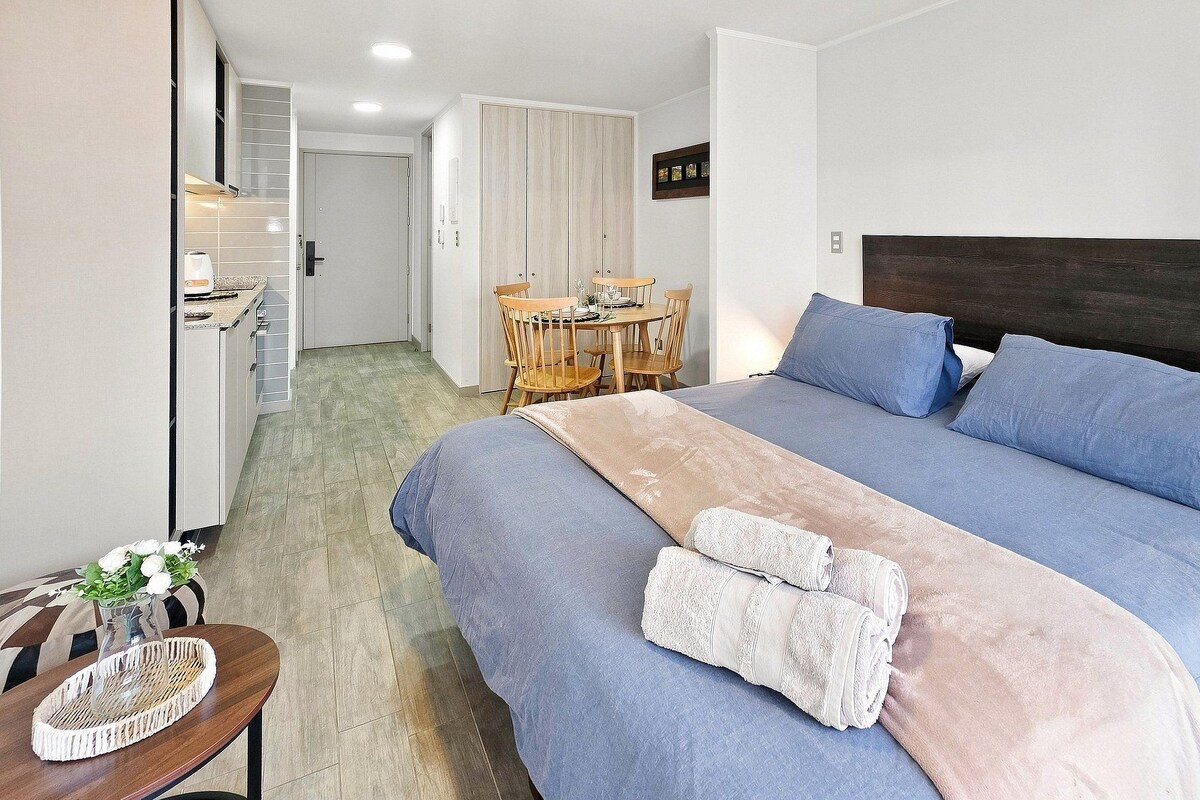Een slaapkamer met een groot bed, een houten eettafel en een stoel.