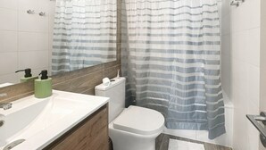 A bathroom with a white sink, a toilet, a shower curtain, and a mirror. - Oceana Suites Eco España (Santiago)