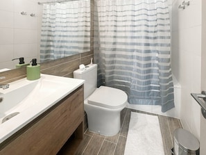 Une salle de bain avec un lavabo blanc, des toilettes, un rideau de douche et un miroir.