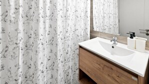 Een badkamer met een houten wastafel, een witte wasbak en een spiegel erboven.
