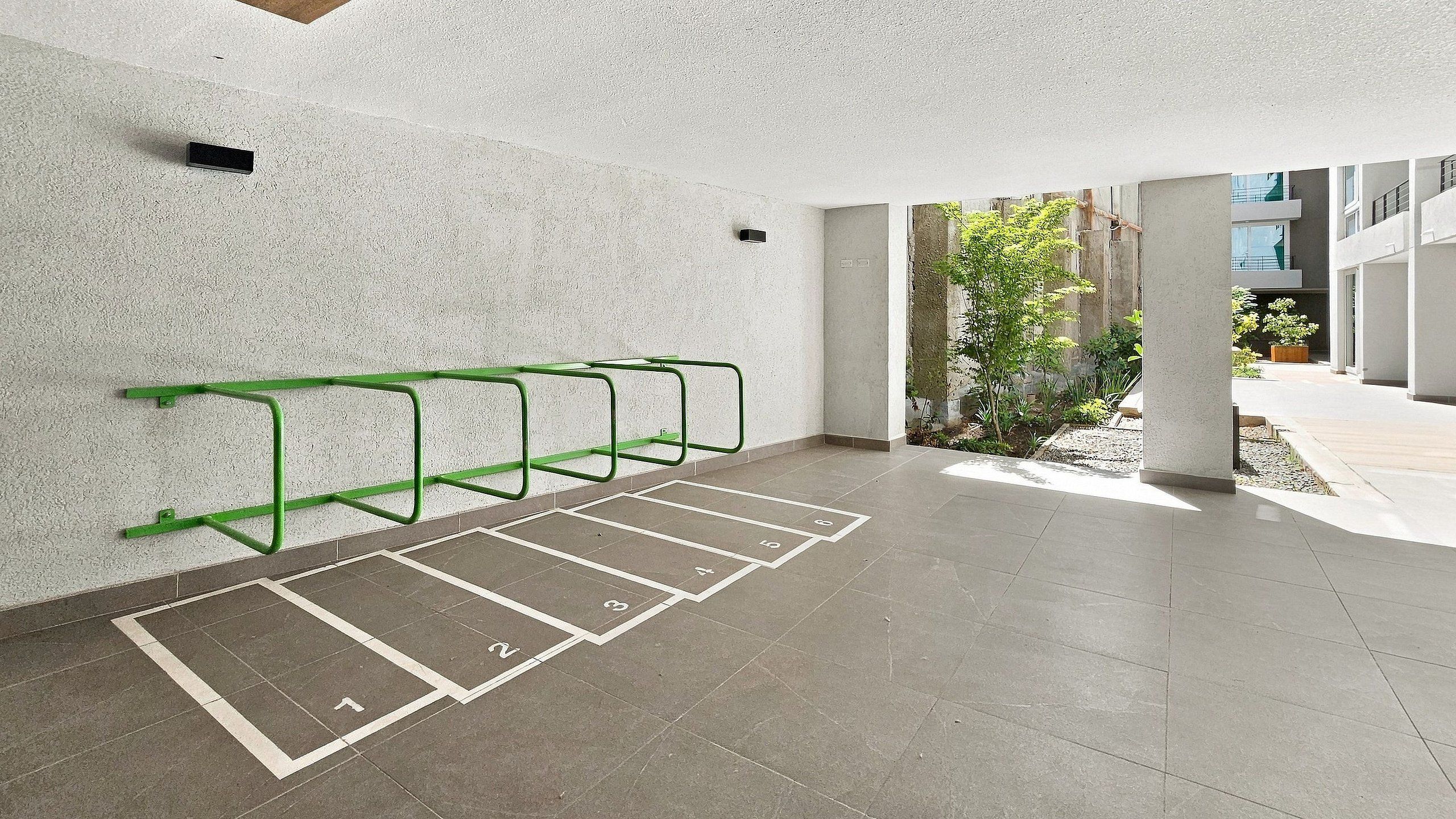 Un área de estacionamiento con espacios delimitados y un aparcamiento de metal verde para bicicletas.